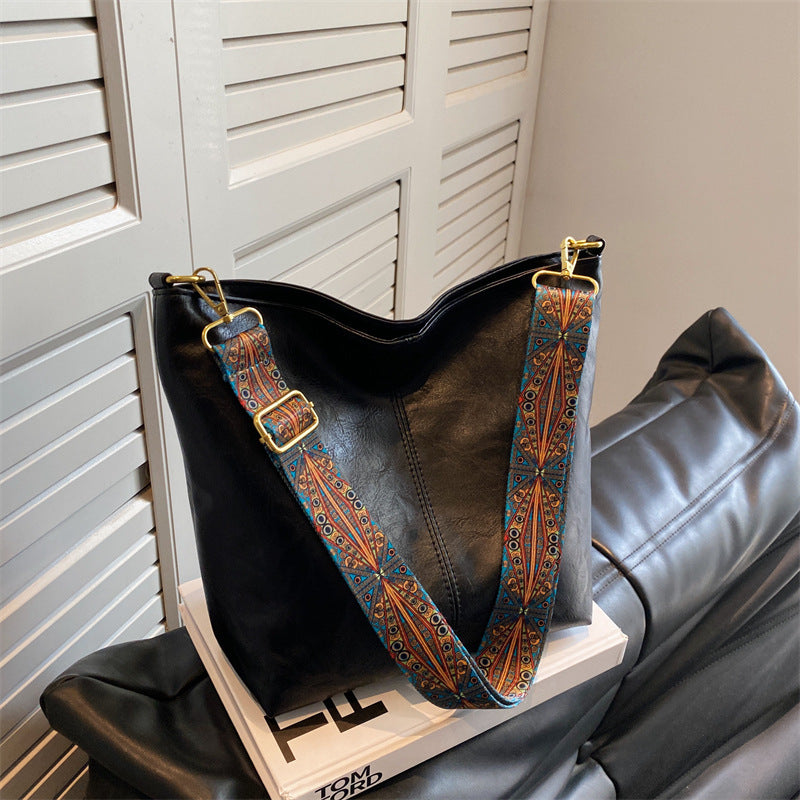 Black leather handbag with a decorative strap on a wooden stand against a neutral background