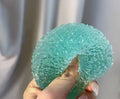 Hand holding a textured teal ball Squishy against a neutral background