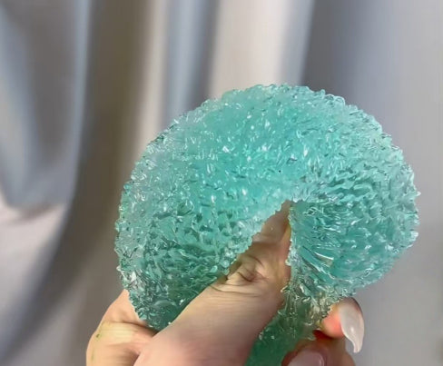 Hand holding a textured teal ball Squishy against a neutral background