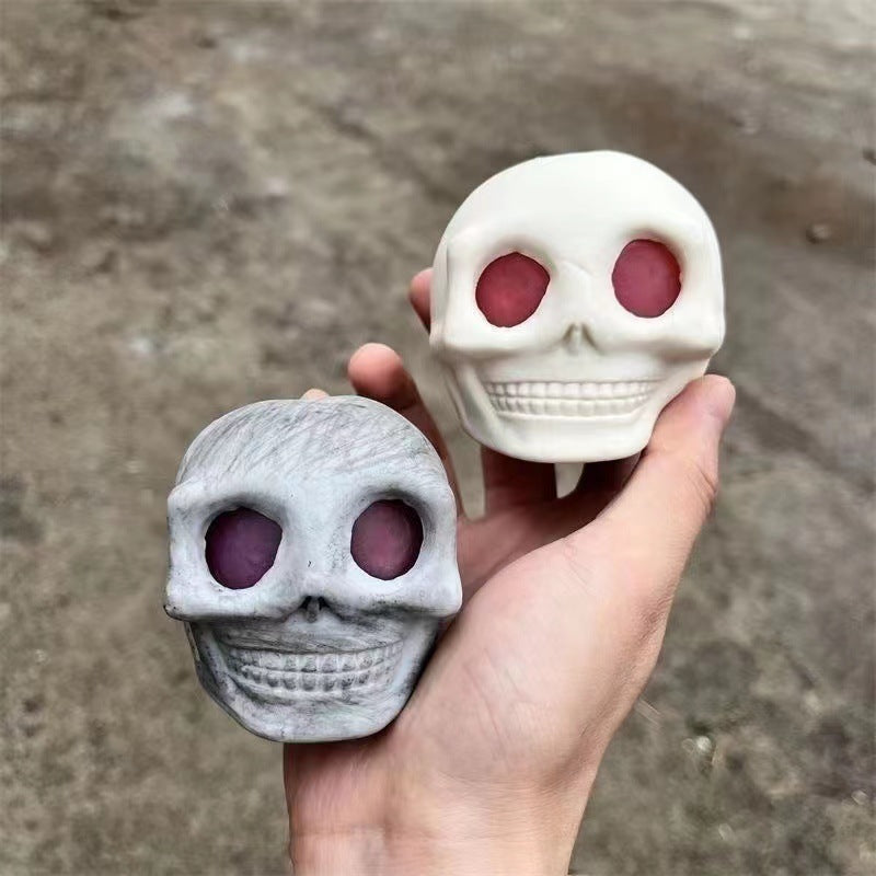 Two small skull-shaped squishy fidget toy stress relief held in a hand against a concrete background