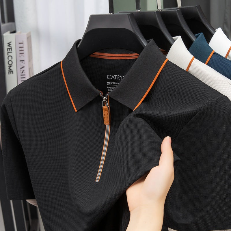 Black polo shirt with orange accents being held by a hand, with other shirts in the background.