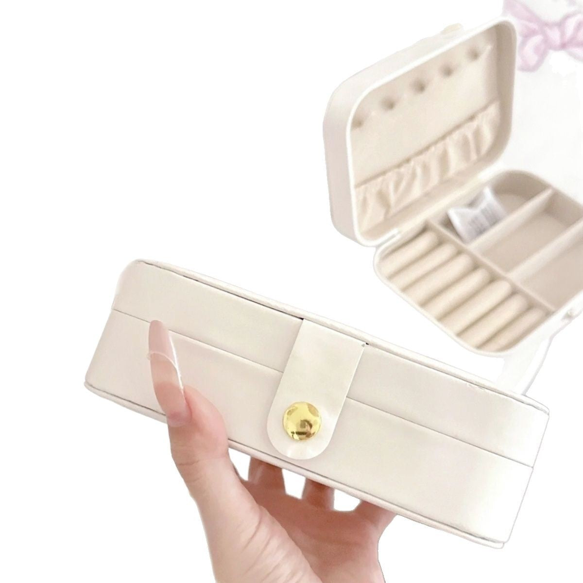 A cream-colored faux leather jewelry organizer case held by a hand, with another open view in the background showing its interior compartments.