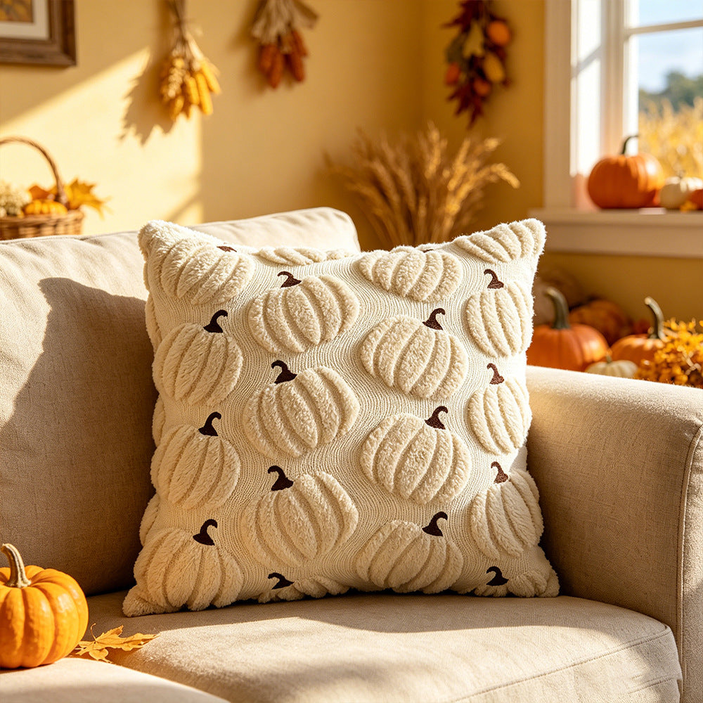 A square cream throw pillow with a 3D textured pumpkin pattern and small dark brown bird accents, styled on a beige sofa in a warm autumn living room setting.
