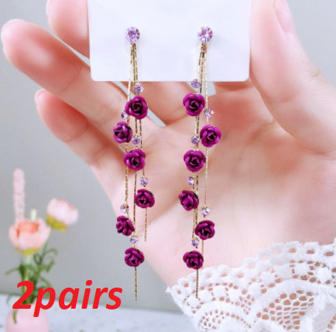 Purple floral earrings held by a hand with a blurred background