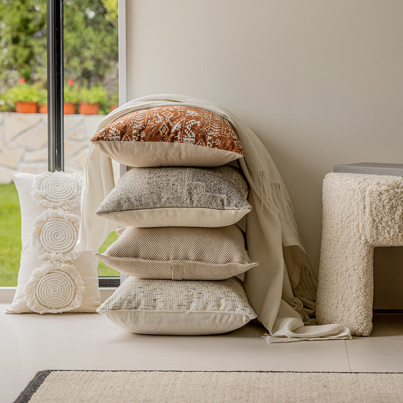 Stack of textured pillows on a windowsill with a neutral color scheme.