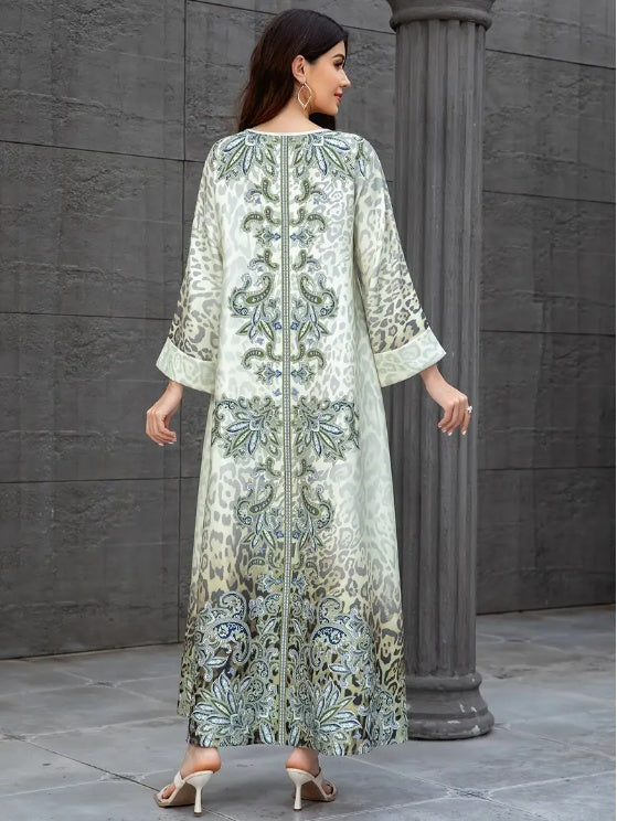 Woman wearing a long, light-colored embroidered dress against a gray stone wall.