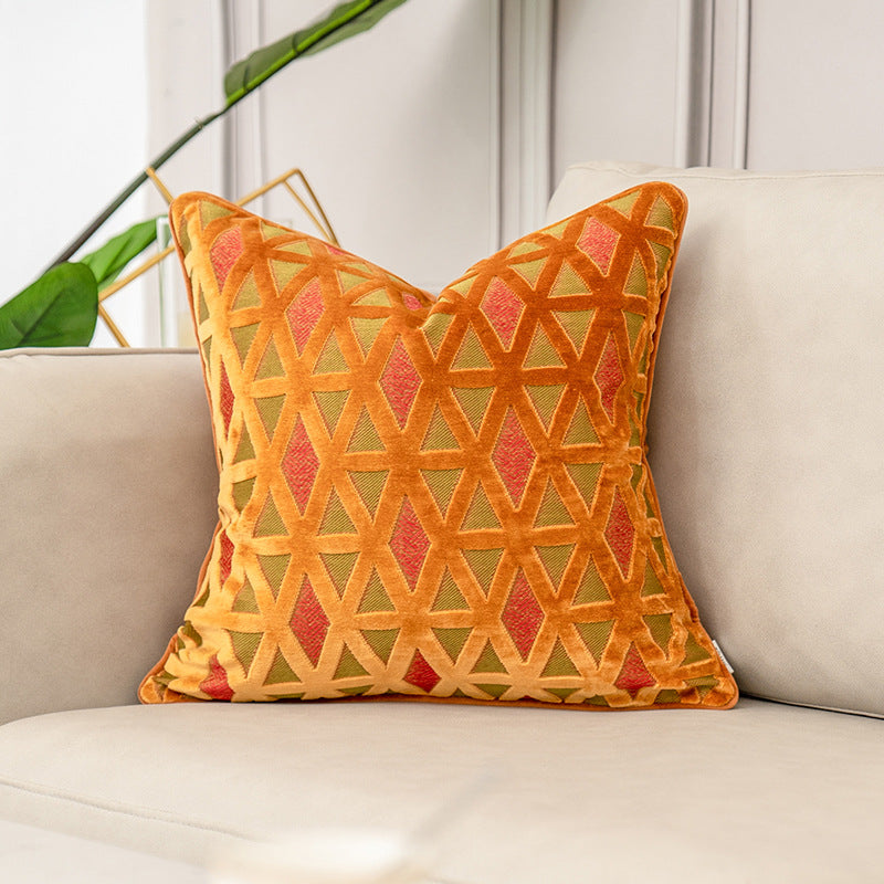 A square decorative throw pillow with a geometric diamond pattern in orange, yellow, and red, styled on a light beige sofa.