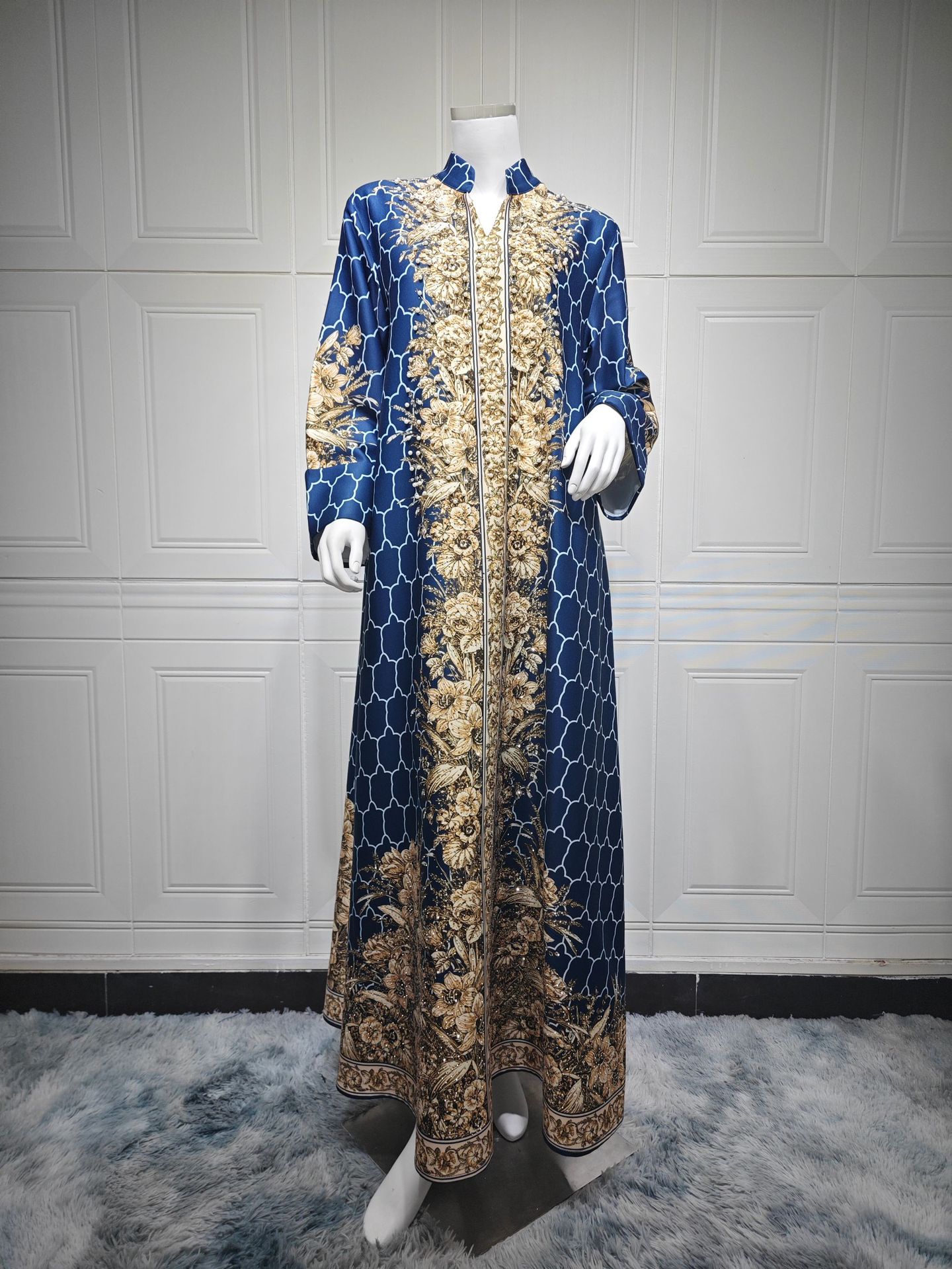 Long blue dress with gold floral patterns on a mannequin against a white paneled wall.