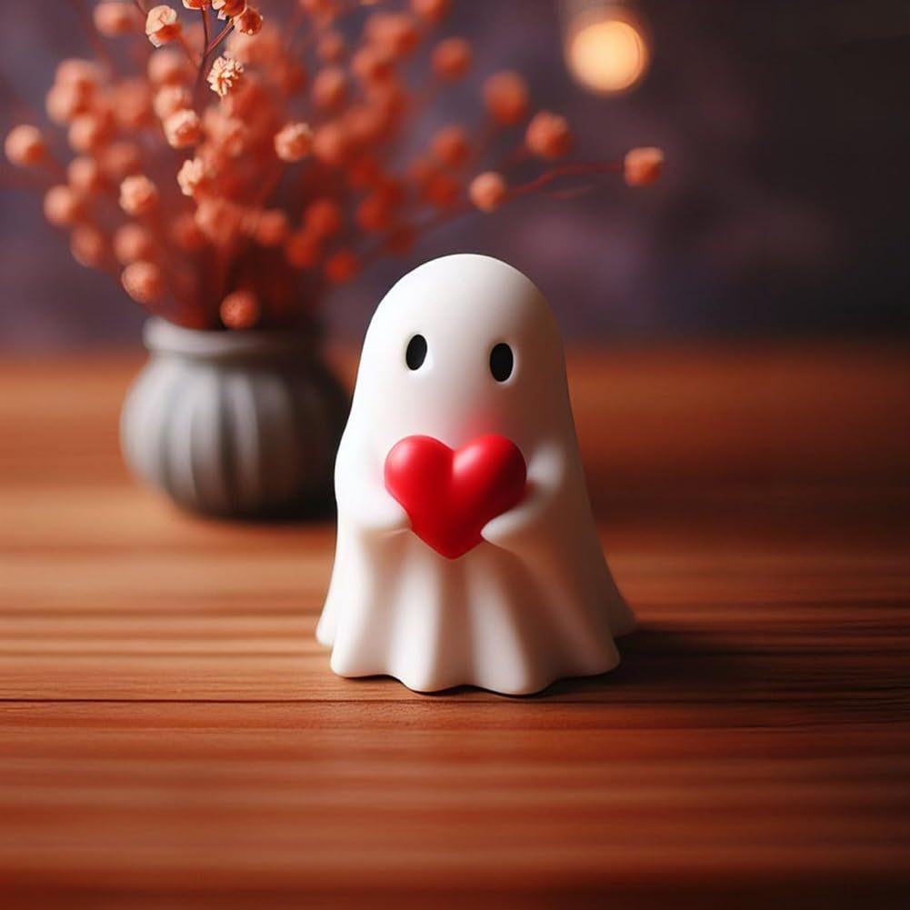 White ghost figurine holding a red heart on a wooden surface with blurred decorative elements in the background.