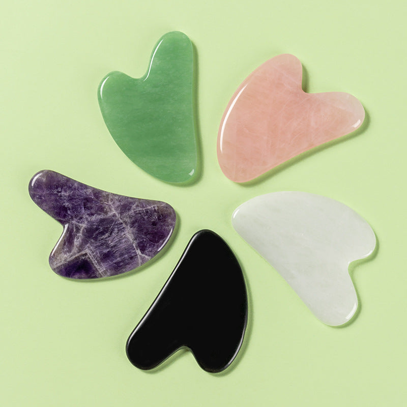 Five heart-shaped gua sha tools in different colors on a light green background