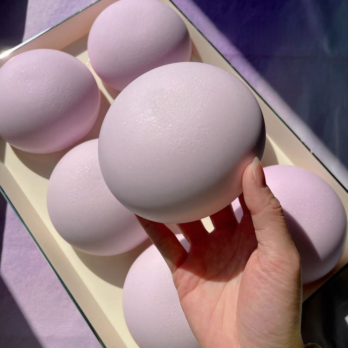 Hand holding a pink makeup sponge with more sponges in the background