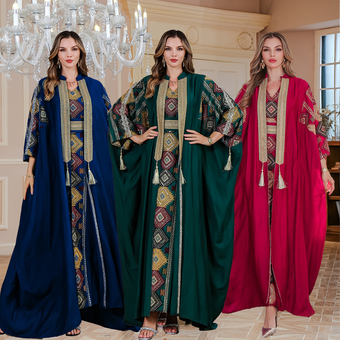Three women wearing colorful abayas in a decorative room with a chandelier.