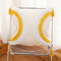 Decorative chair with white cushions and yellow fringe on a wooden floor.