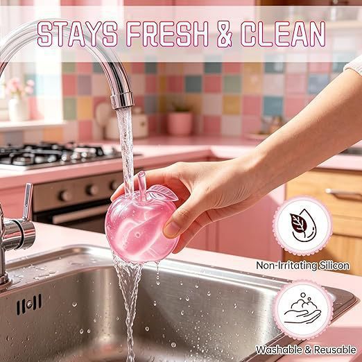 Hand washing a pink silicone apple squishy under running water in a kitchen sink with text 'Stays Fresh & Clean' and icons indicating non-irritating silicon, washable, and reusable.