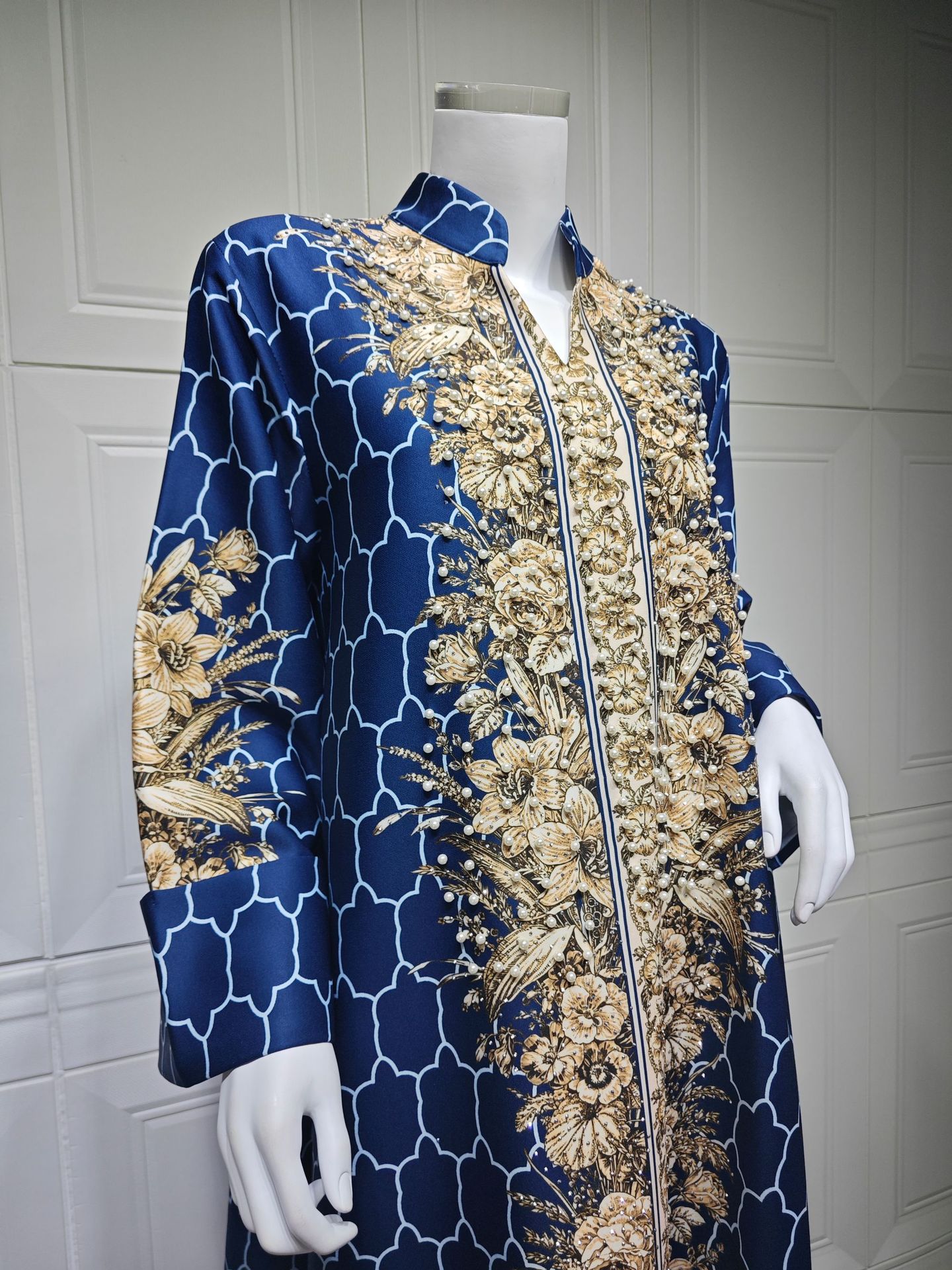 Blue and gold embroidered jacket on a mannequin against a white paneled wall.