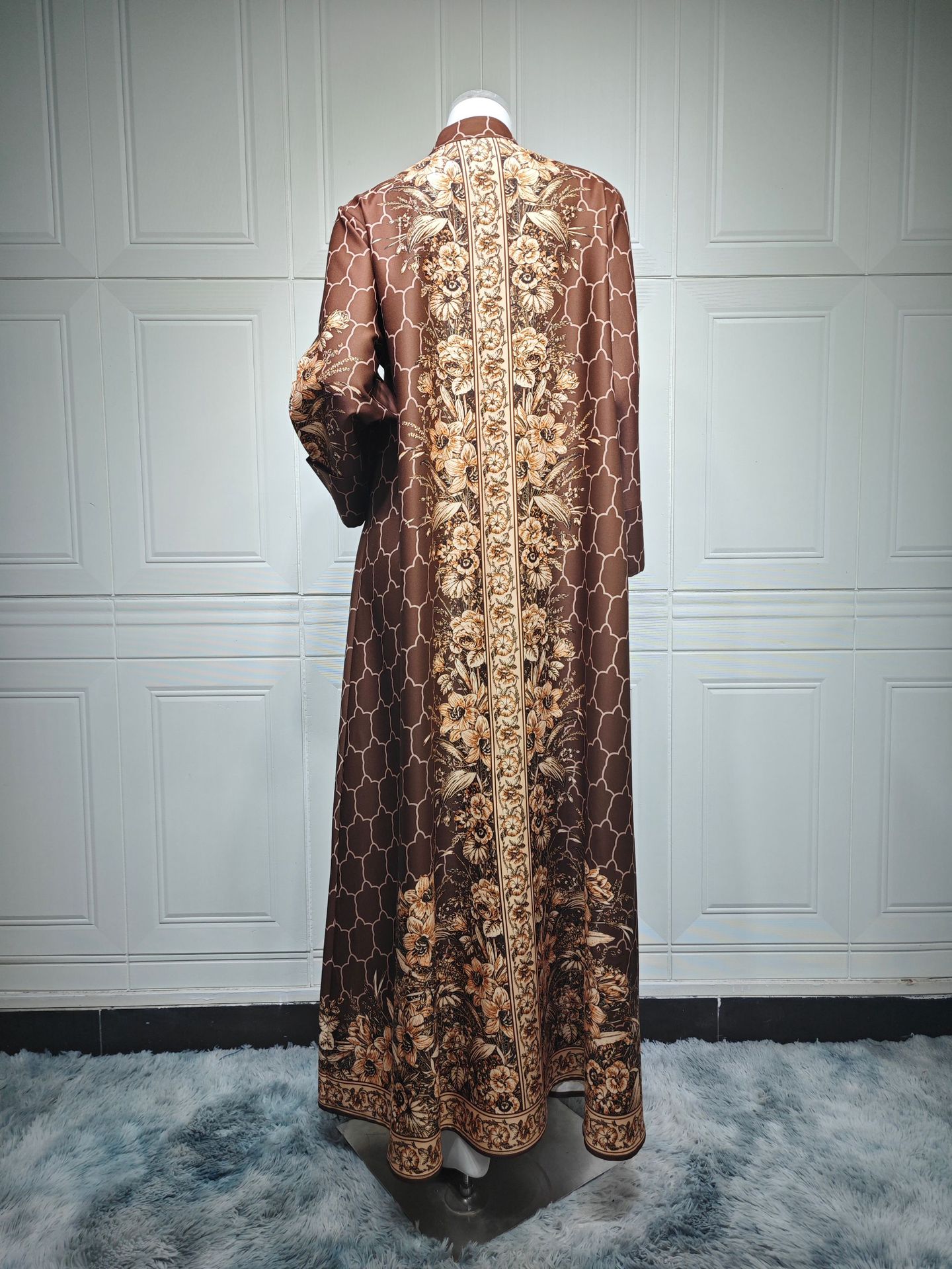 Long, ornate coat with intricate patterns on a mannequin against a white paneled wall.