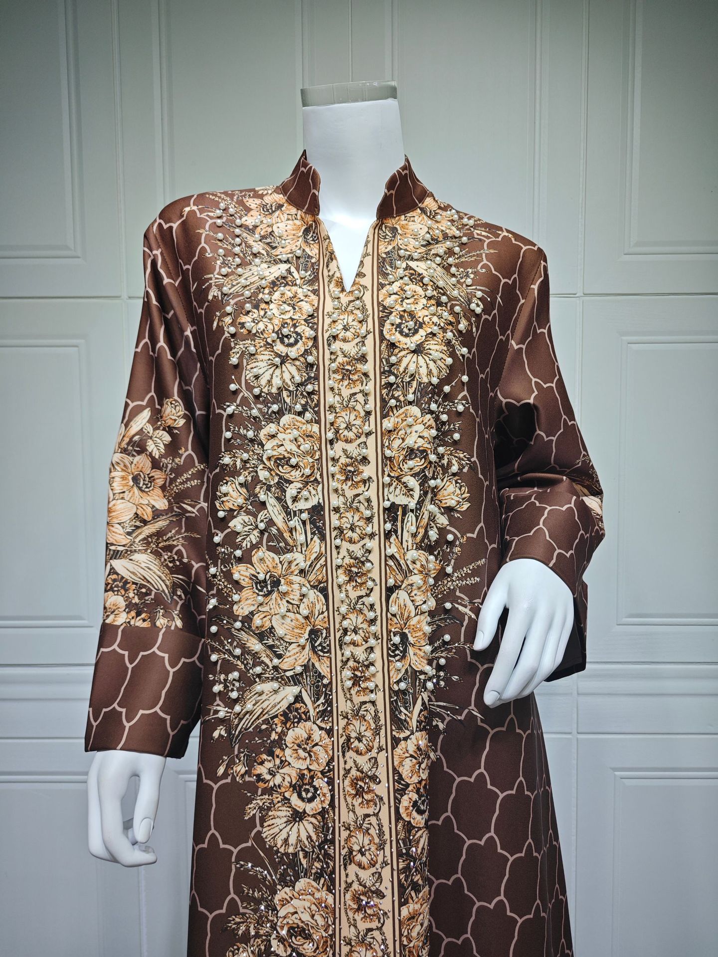 Mannequin wearing a patterned brown and gold garment against a white paneled wall.