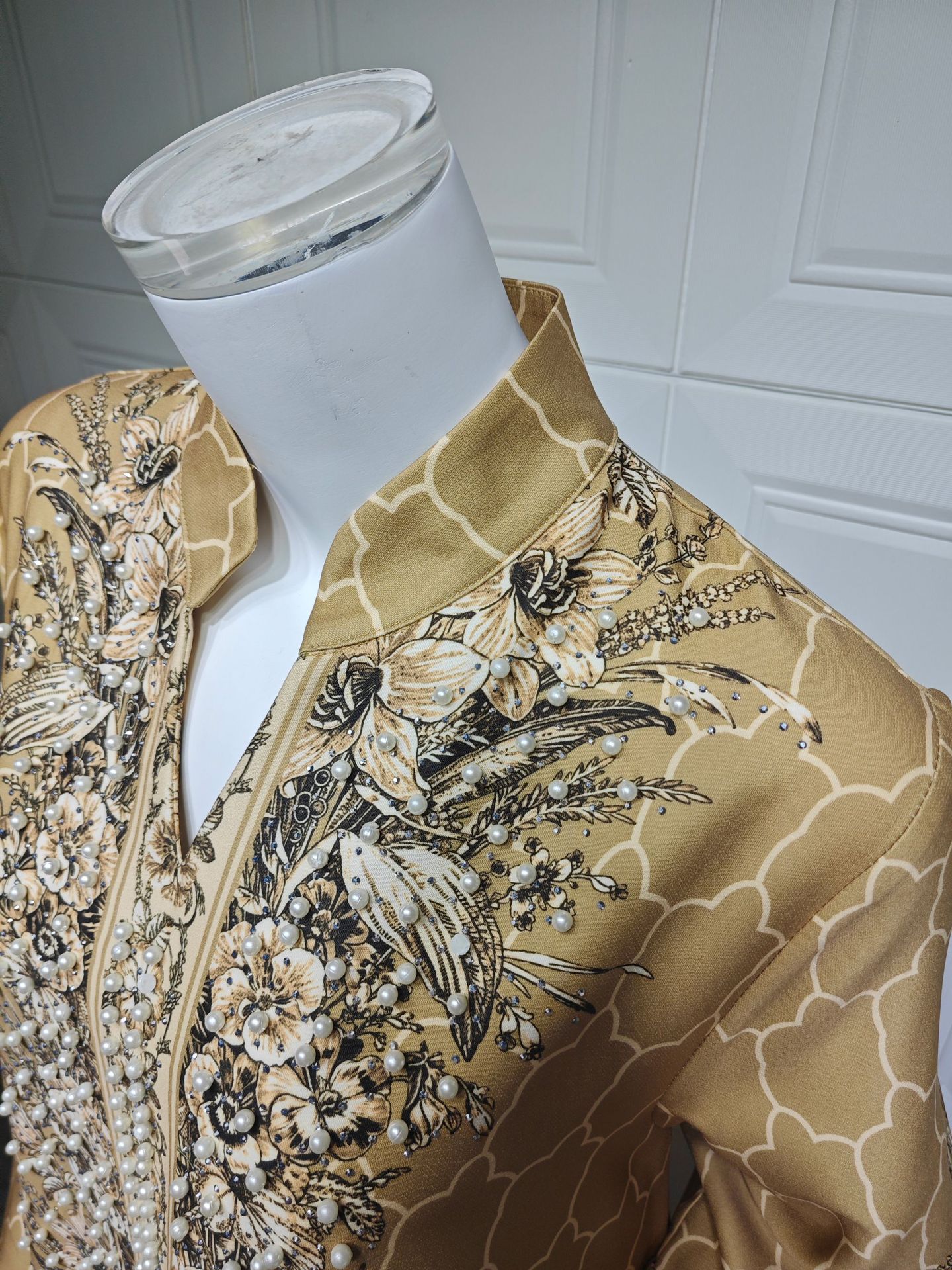 Mannequin wearing a gold floral patterned outfit against a white paneled wall.