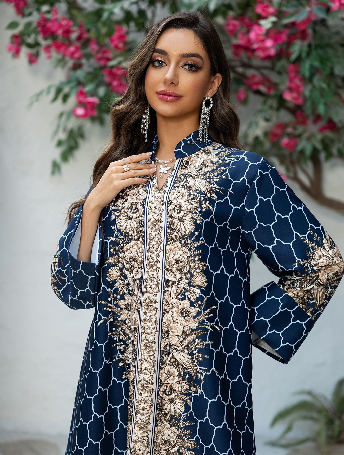 Woman wearing a navy blue and gold embroidered dress with floral patterns, standing against a light background with pink flowers.