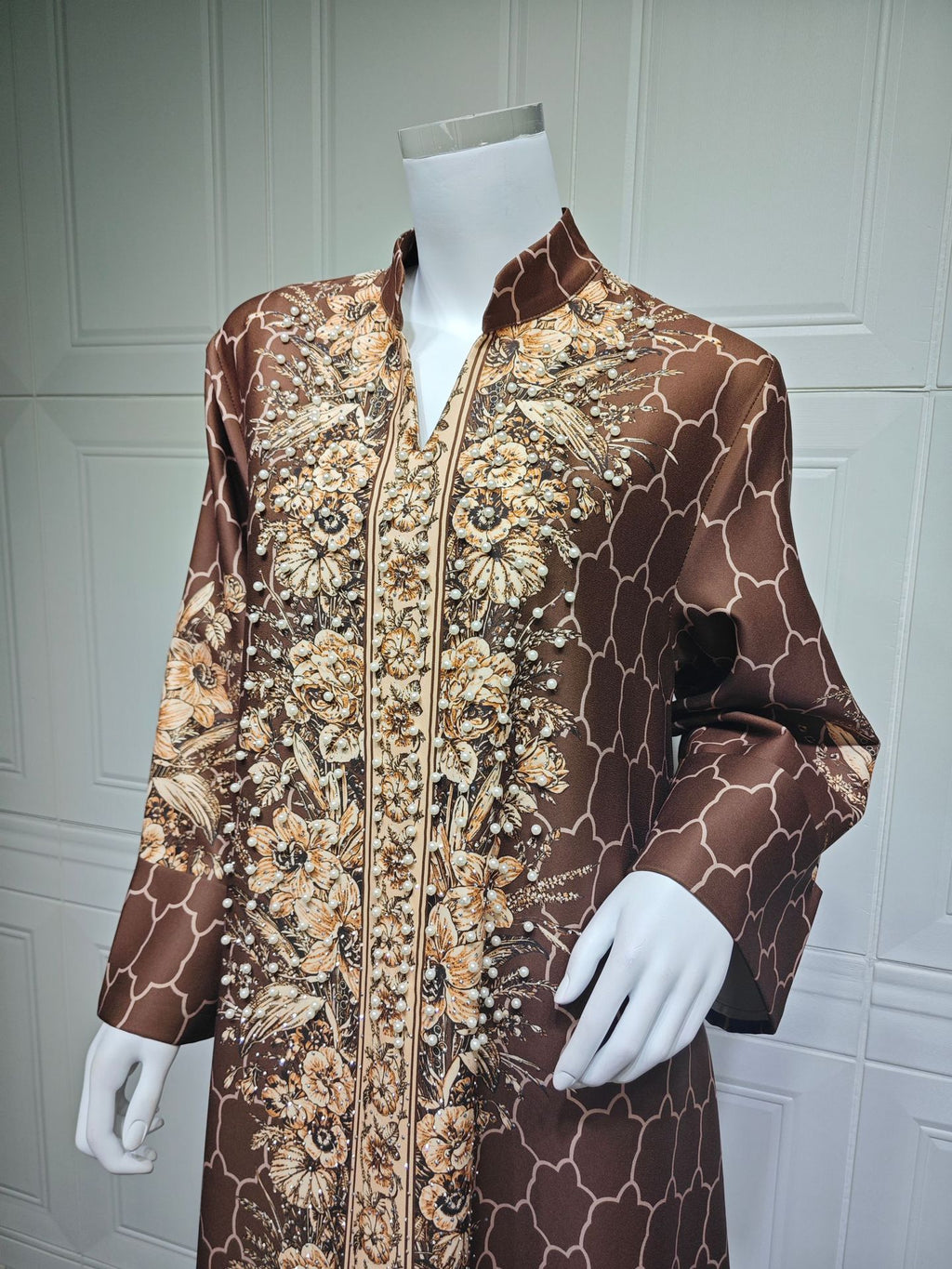 Mannequin wearing a brown and gold patterned coat against a white paneled wall.