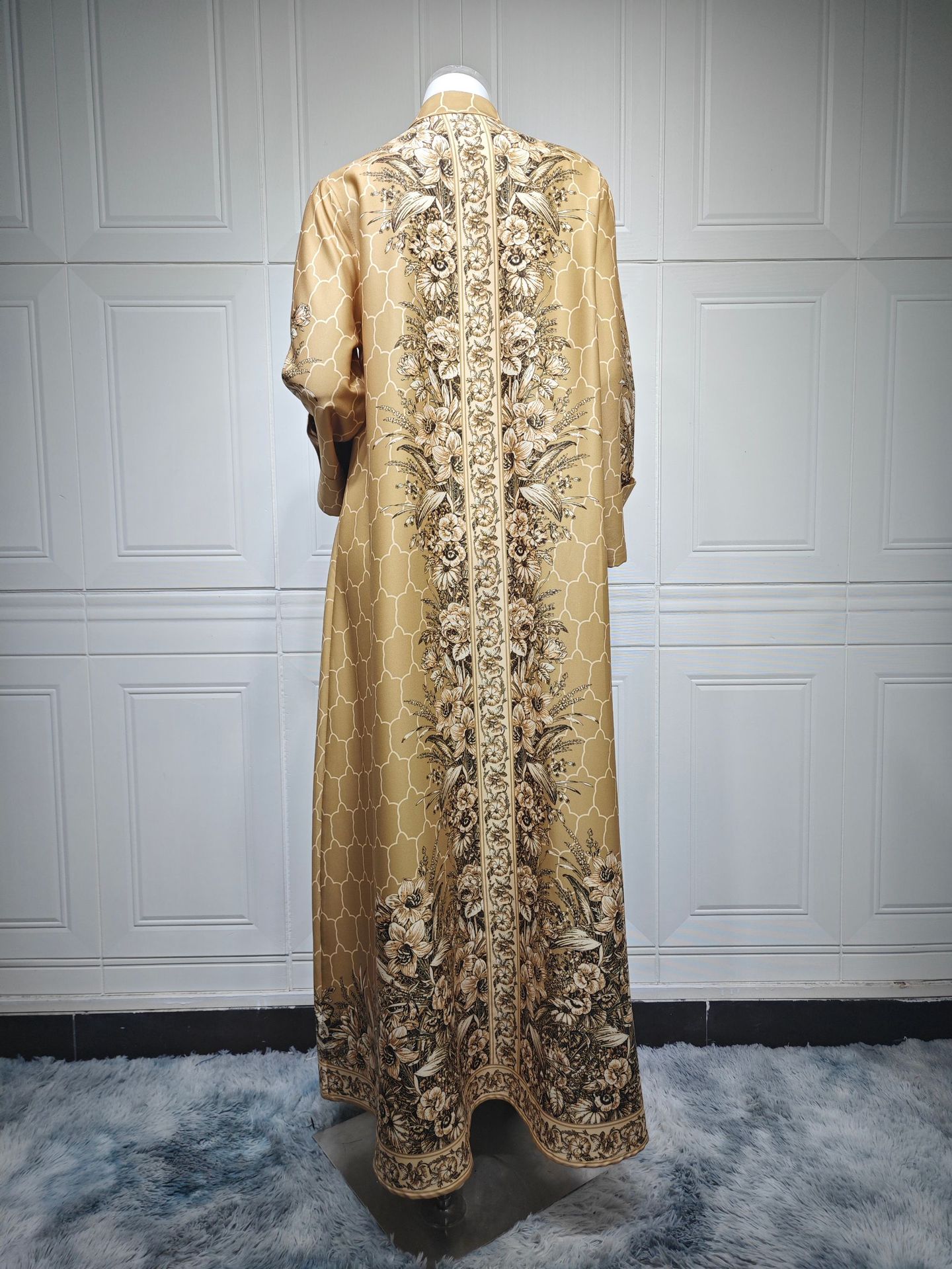 Long, ornate dress with intricate patterns on a white paneled wall background