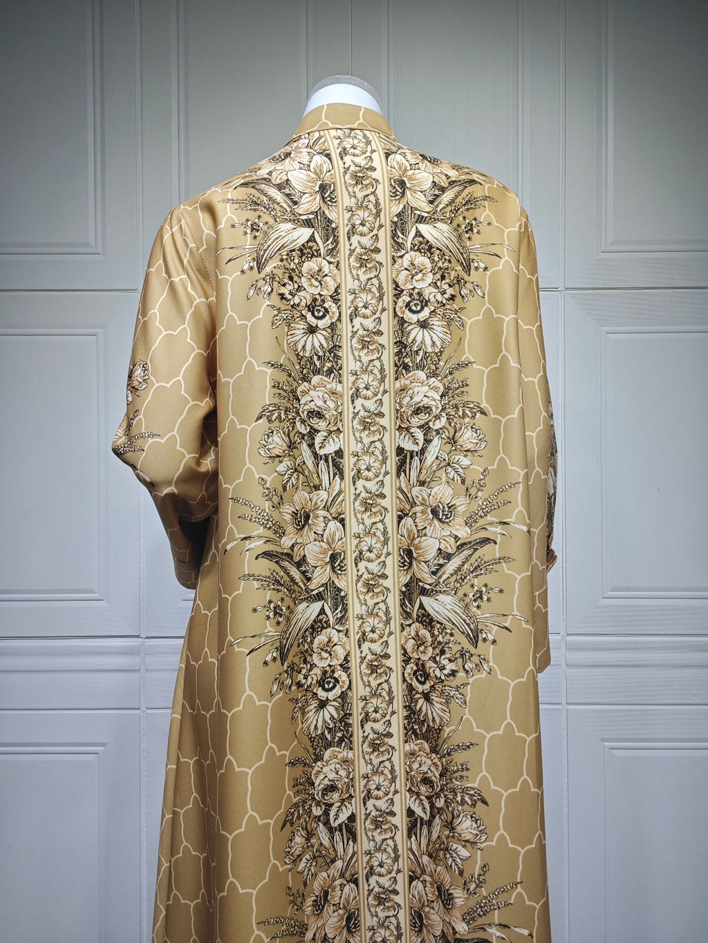 Beige embroidered garment on a mannequin against a gray paneled wall