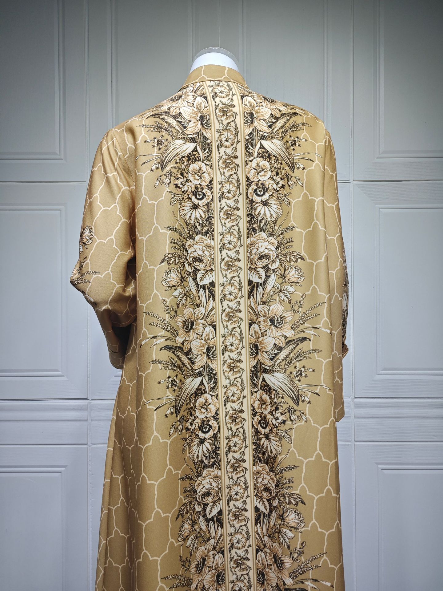 Beige embroidered garment on a mannequin against a gray paneled wall